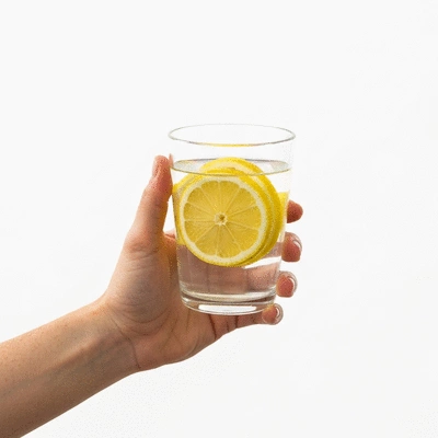 Person holding a glass of water with lemon slices, representing hydration